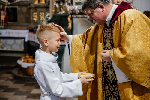 Proboszcz wykonujący znak krzyża na czole dziecka, które przyniosło komunikanty
